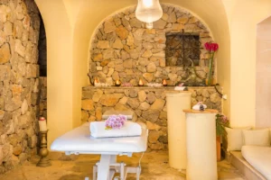 Privater Massageraum mit mediterranen Steinwänden und warmen Licht mit Massageliege und kleinem Sofa.